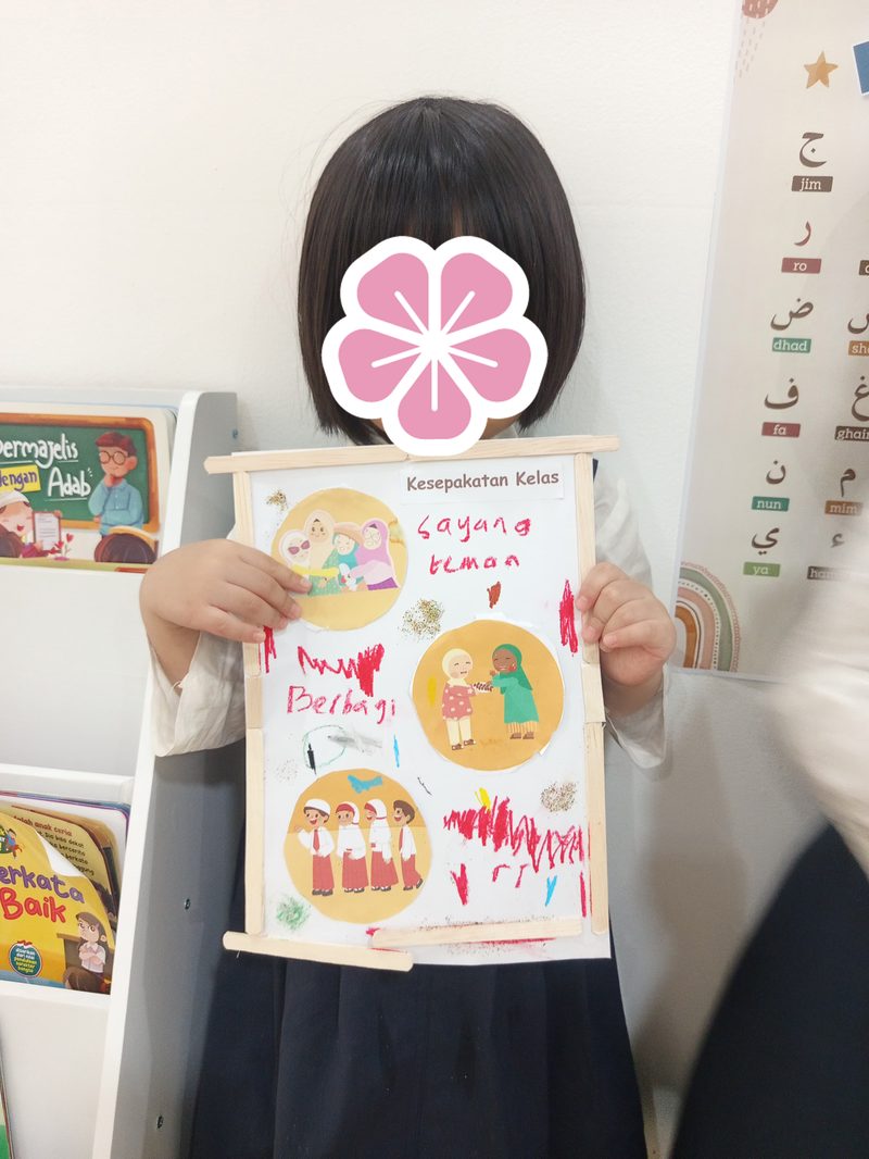 Anak menunjukkan poster kesepakatan kelas tentang sayang teman